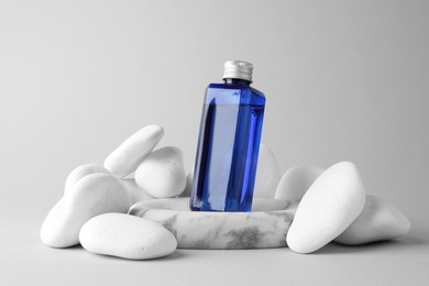 Photo of Bottle of cosmetic product and stones on light grey background