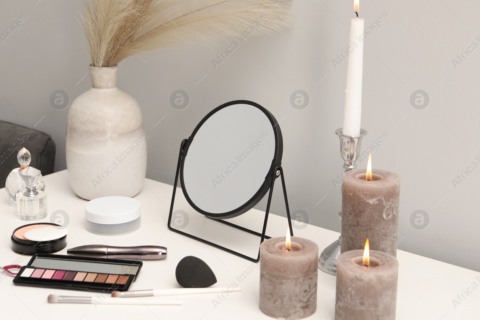 Photo of Dressing table with mirror, cosmetic products, perfumes and burning candles in makeup room