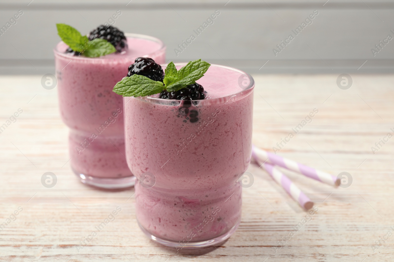 Photo of Glasses of blackberry smoothie with mint and berries on light wooden table, closeup