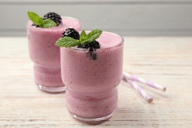 Photo of Glasses of blackberry smoothie with mint and berries on light wooden table, closeup