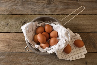 Photo of Chicken eggs in colander with napkin on wooden table, flat lay