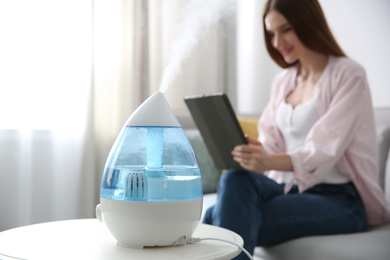 Photo of Modern air humidifier and blurred woman on background