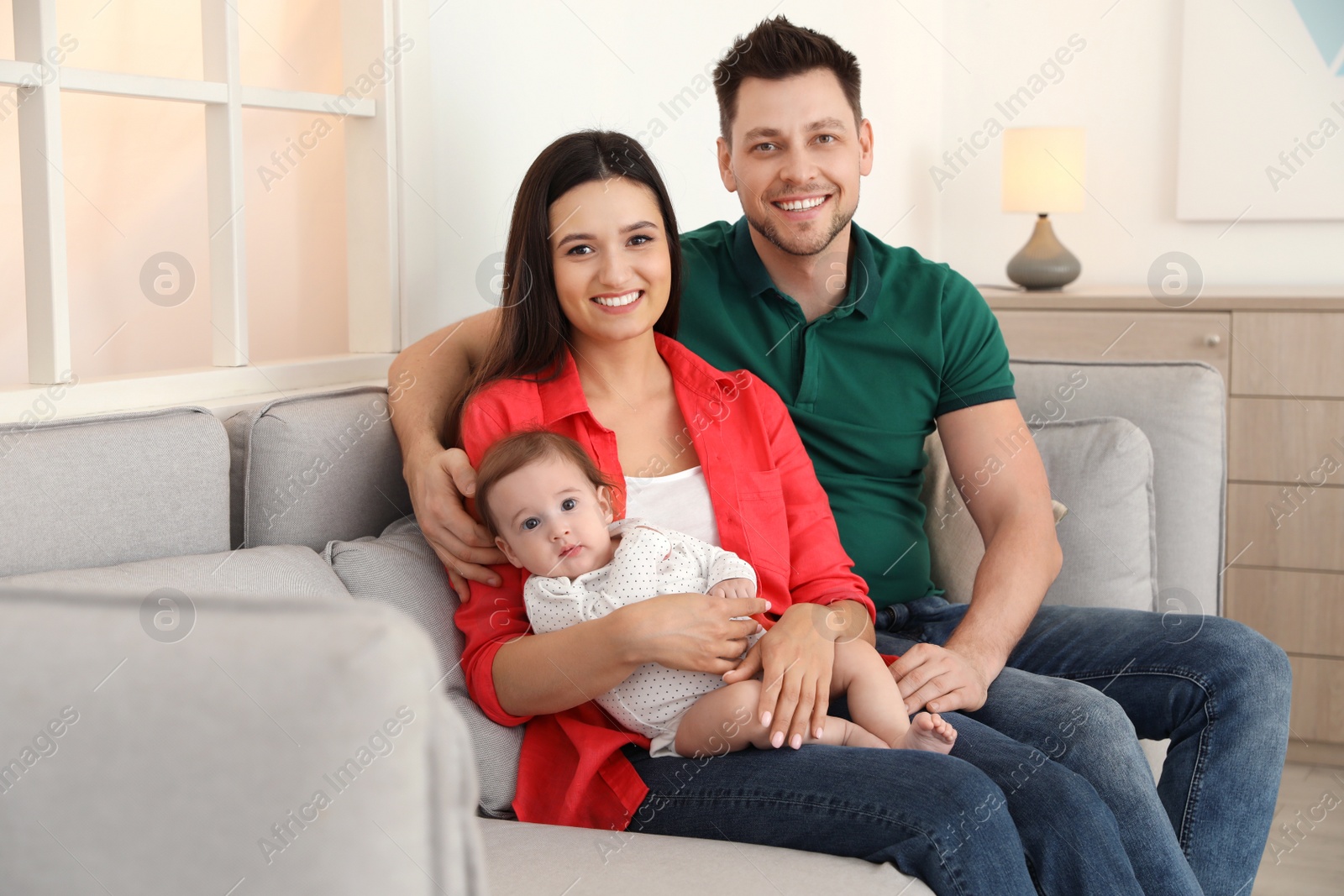 Photo of Happy couple with adorable baby on sofa at home. Family time