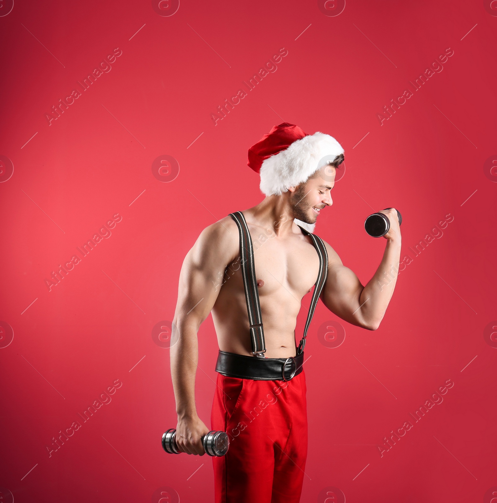 Photo of Shirtless sexy young Santa Claus with dumbbells on color background