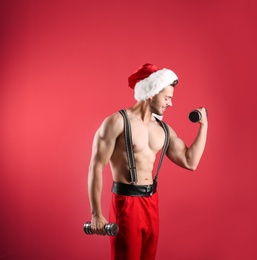 Photo of Shirtless sexy young Santa Claus with dumbbells on color background