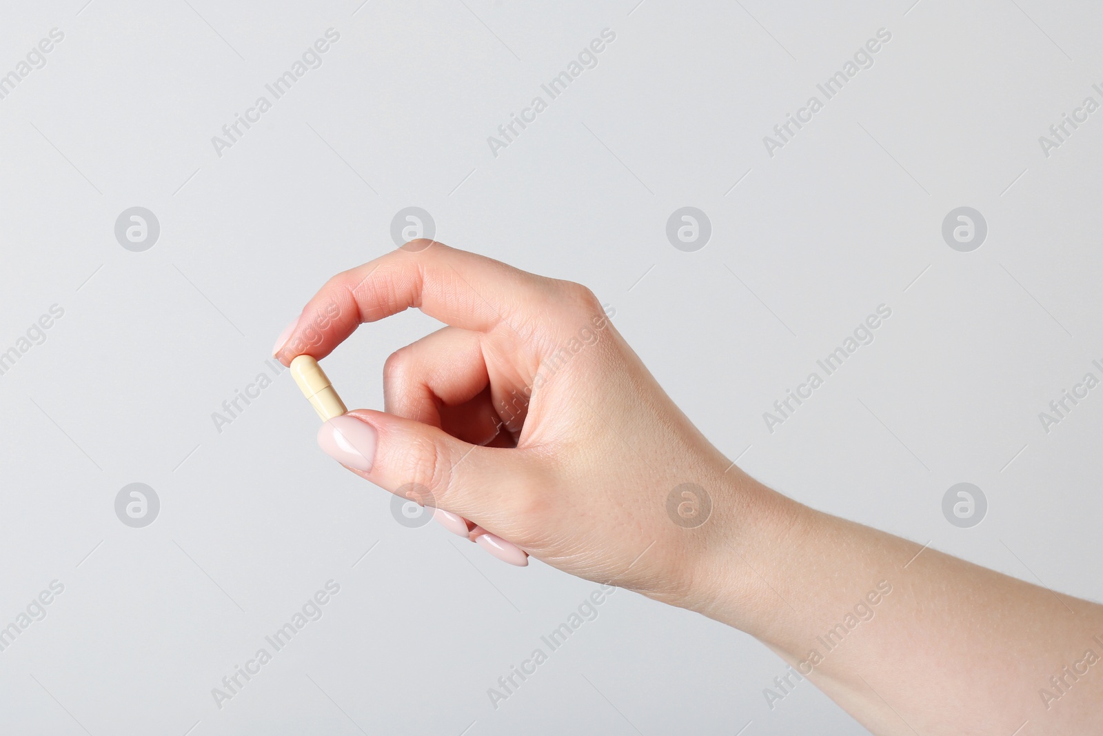 Photo of Woman holding vitamin capsule on light grey background, closeup. Health supplement