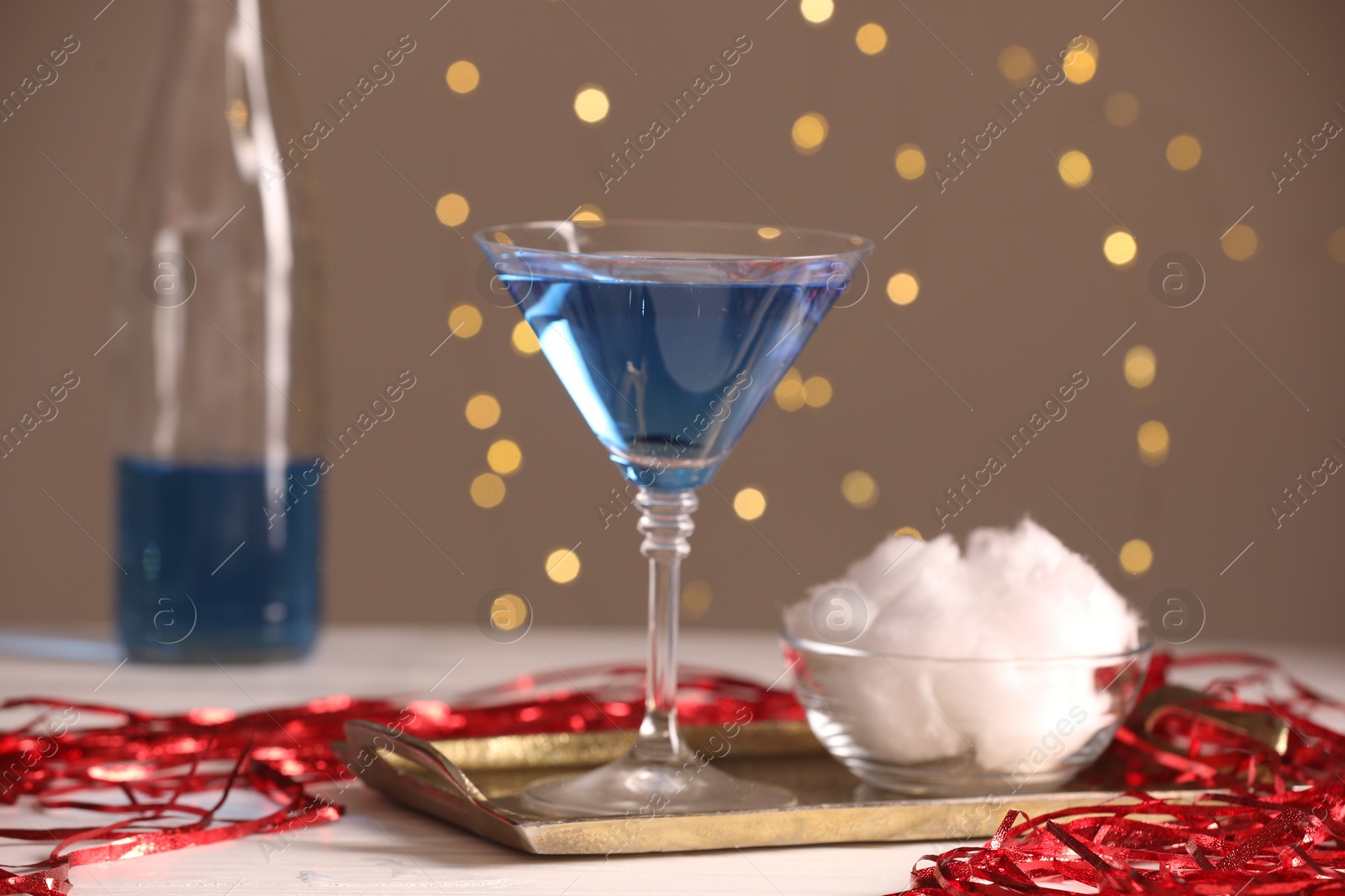 Photo of Tasty cocktail and cotton candy on white table against beige background with blurred lights, closeup