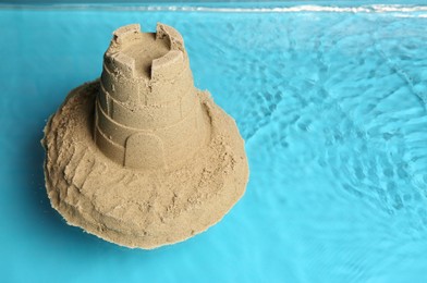 Pile of sand with tower on rippled water, space for text. Beautiful castle