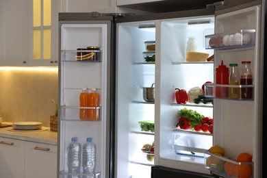 Open refrigerator full of different products in kitchen