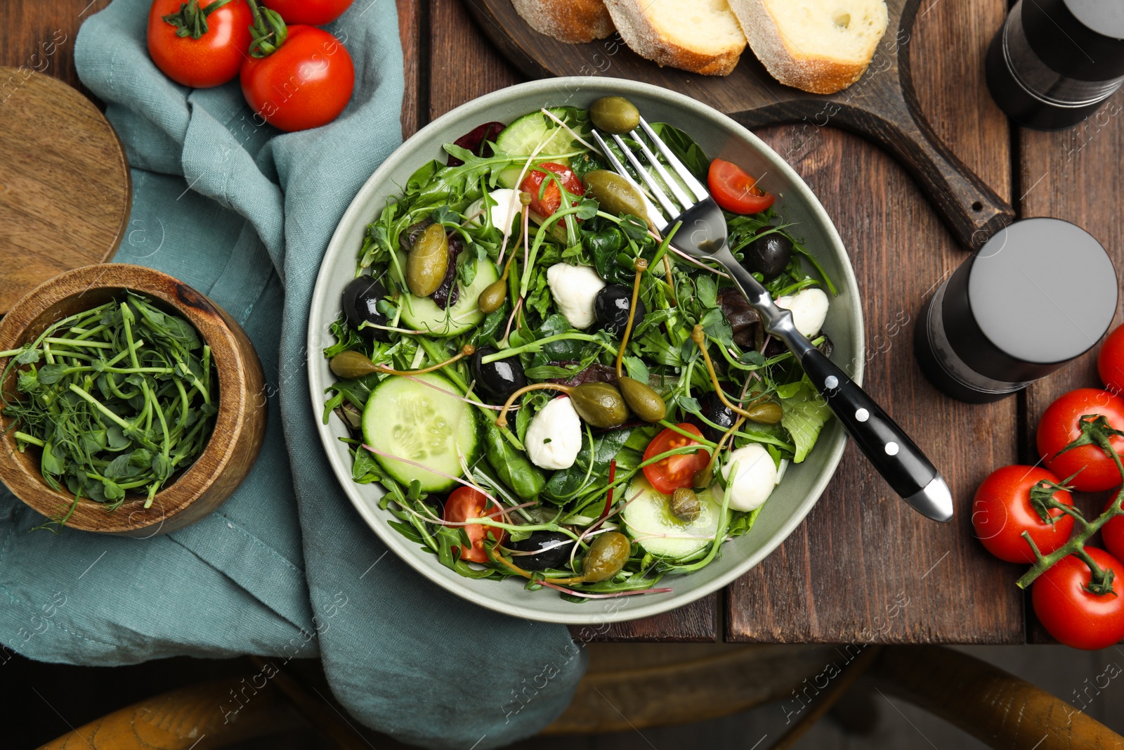 Photo of Fresh salad with vegetables, capers and mozzarella in bowl on wooden table, flat lay
