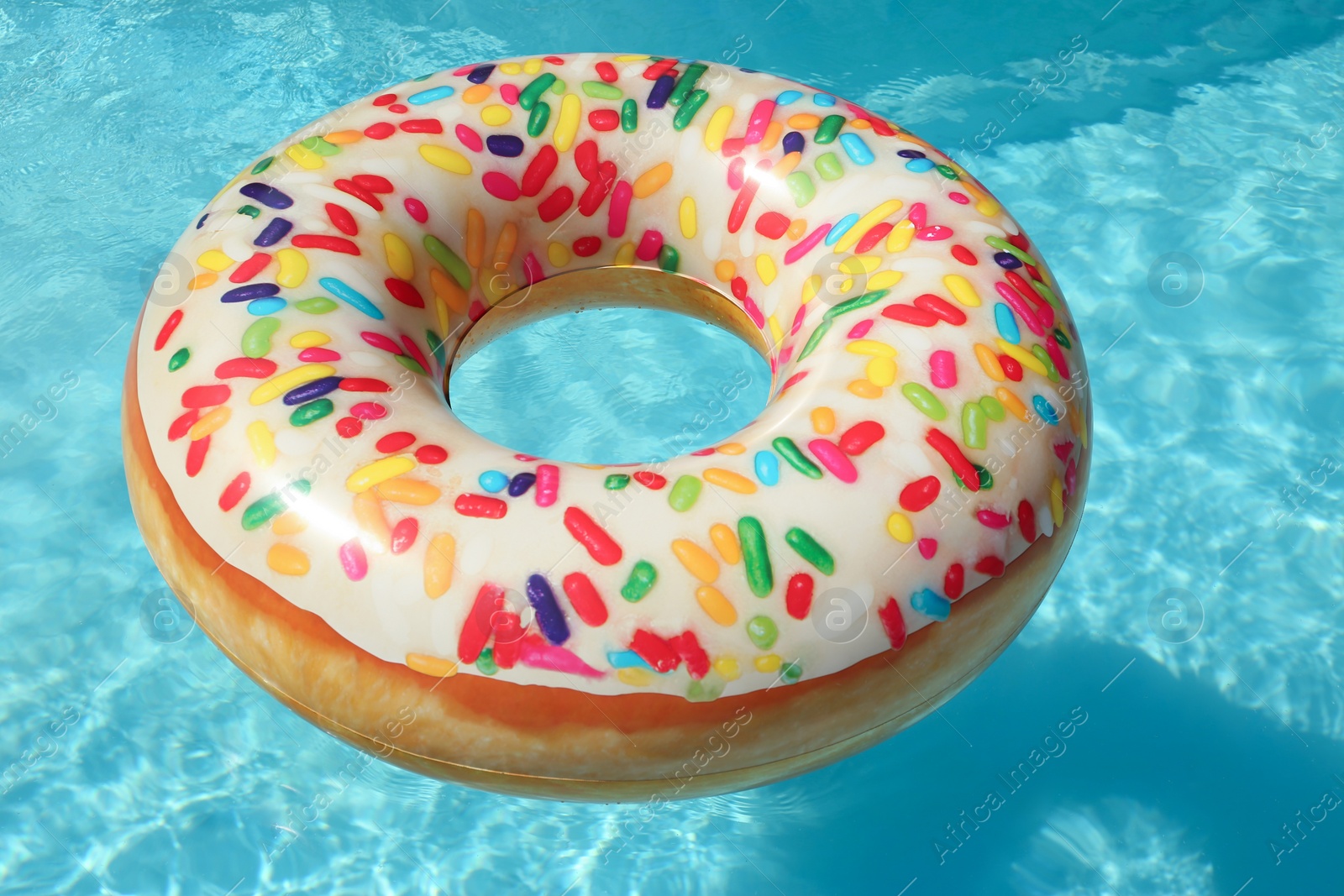 Photo of Bright inflatable doughnut ring floating in swimming pool on sunny day