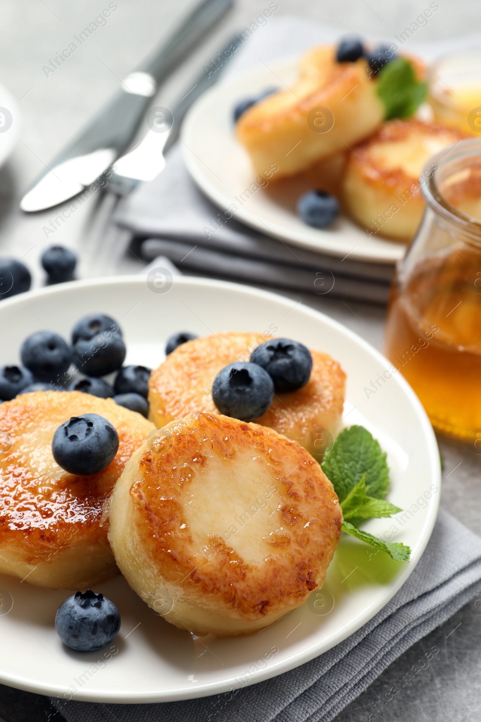 Photo of Delicious cottage cheese pancakes with blueberries, mint and honey on light grey table, closeup