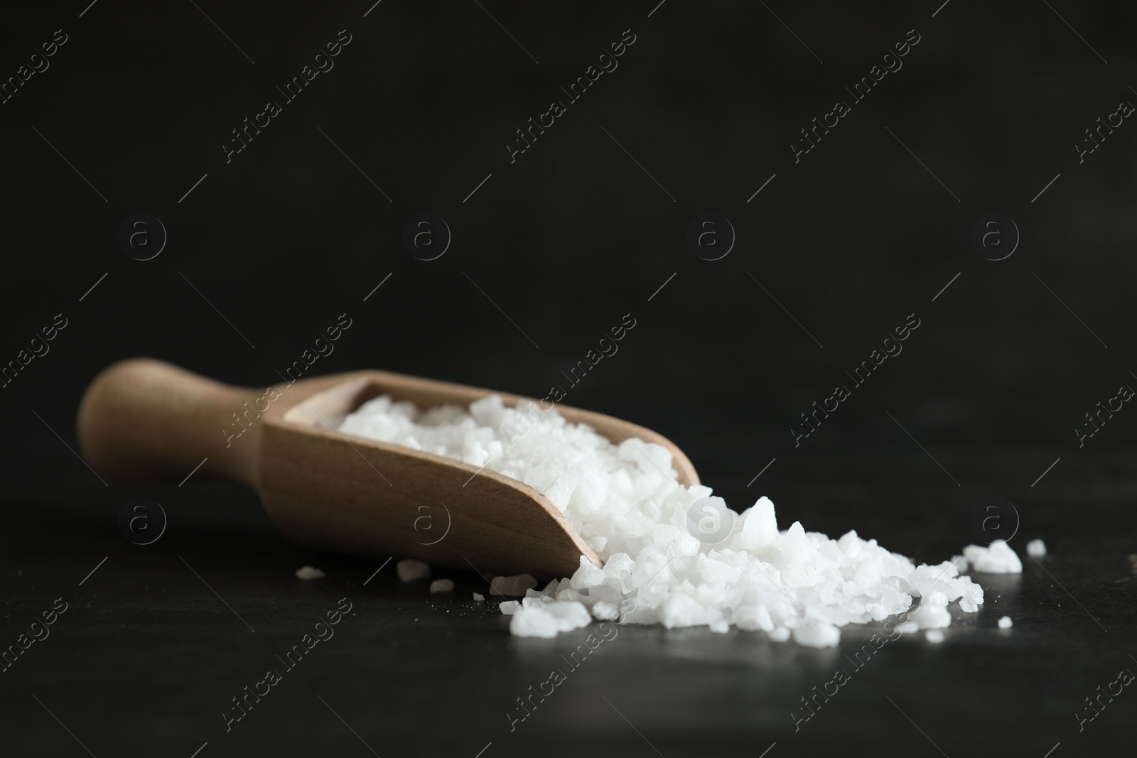 Photo of Organic salt and wooden scoop on black table, closeup. Space for text