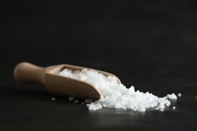 Photo of Organic salt and wooden scoop on black table, closeup. Space for text