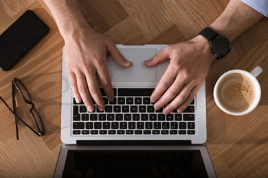 Photo of Man with laptop, cup of coffee and smartphone at wooden table, top view