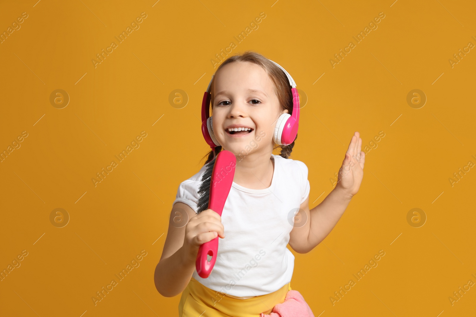 Photo of Cute little girl in headphones with brush singing on orange background