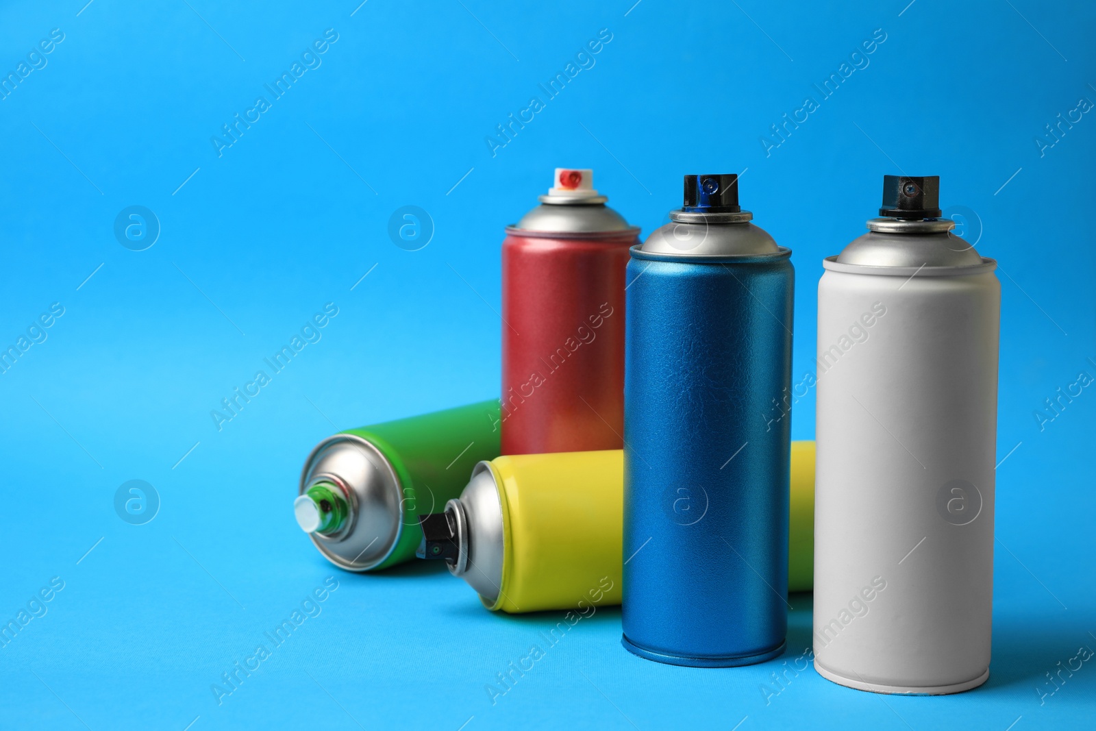 Photo of Cans of different graffiti spray paints on light blue background, space for text