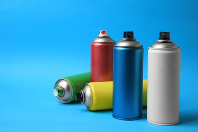 Cans of different graffiti spray paints on light blue background, space for text