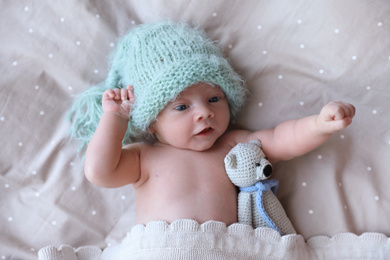 Photo of Cute newborn baby in warm hat with toy lying on bed, top view