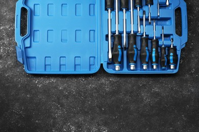 Set of screwdrivers in open toolbox on dark textured table, top view. Space for text