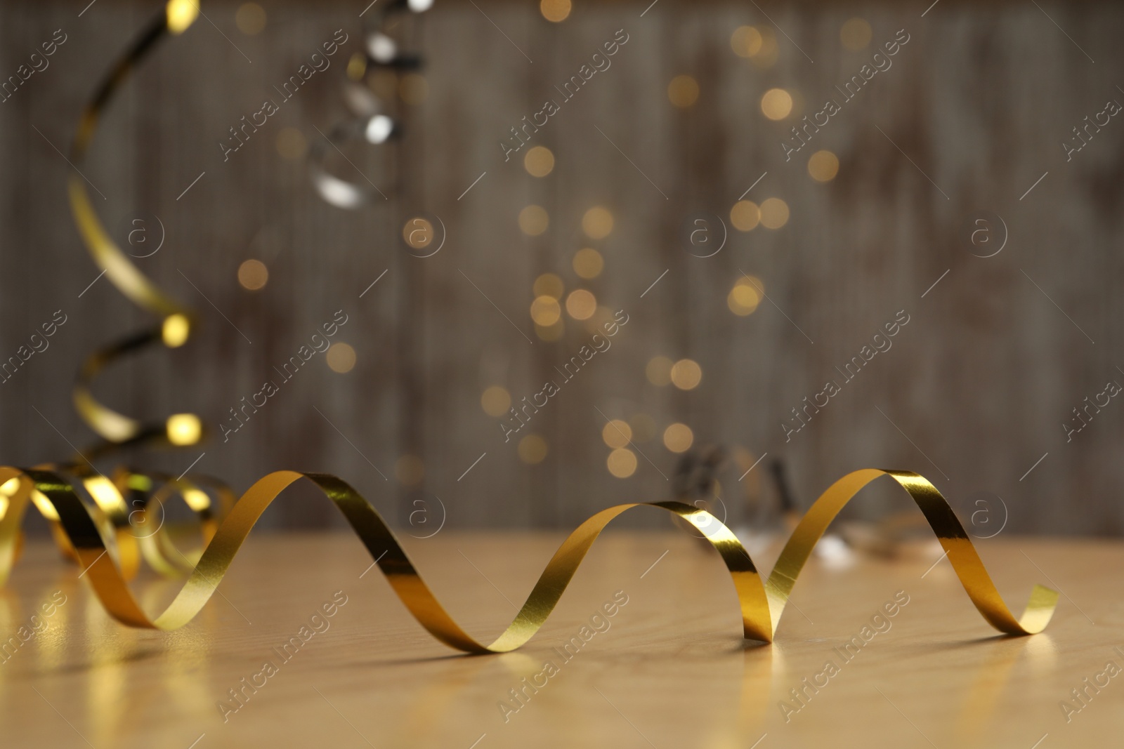 Photo of Shiny golden serpentine streamer on wooden table against blurred lights. Space for text