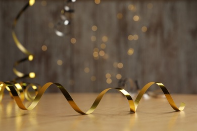 Shiny golden serpentine streamer on wooden table against blurred lights. Space for text