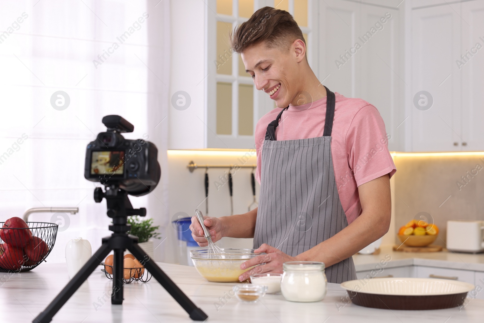Photo of Smiling food blogger cooking while recording video in kitchen