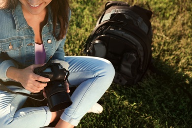 Young female photographer holding professional camera and sitting on grass outdoors