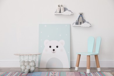 Poster with bear, chair and basket near light wall in baby room. Interior design