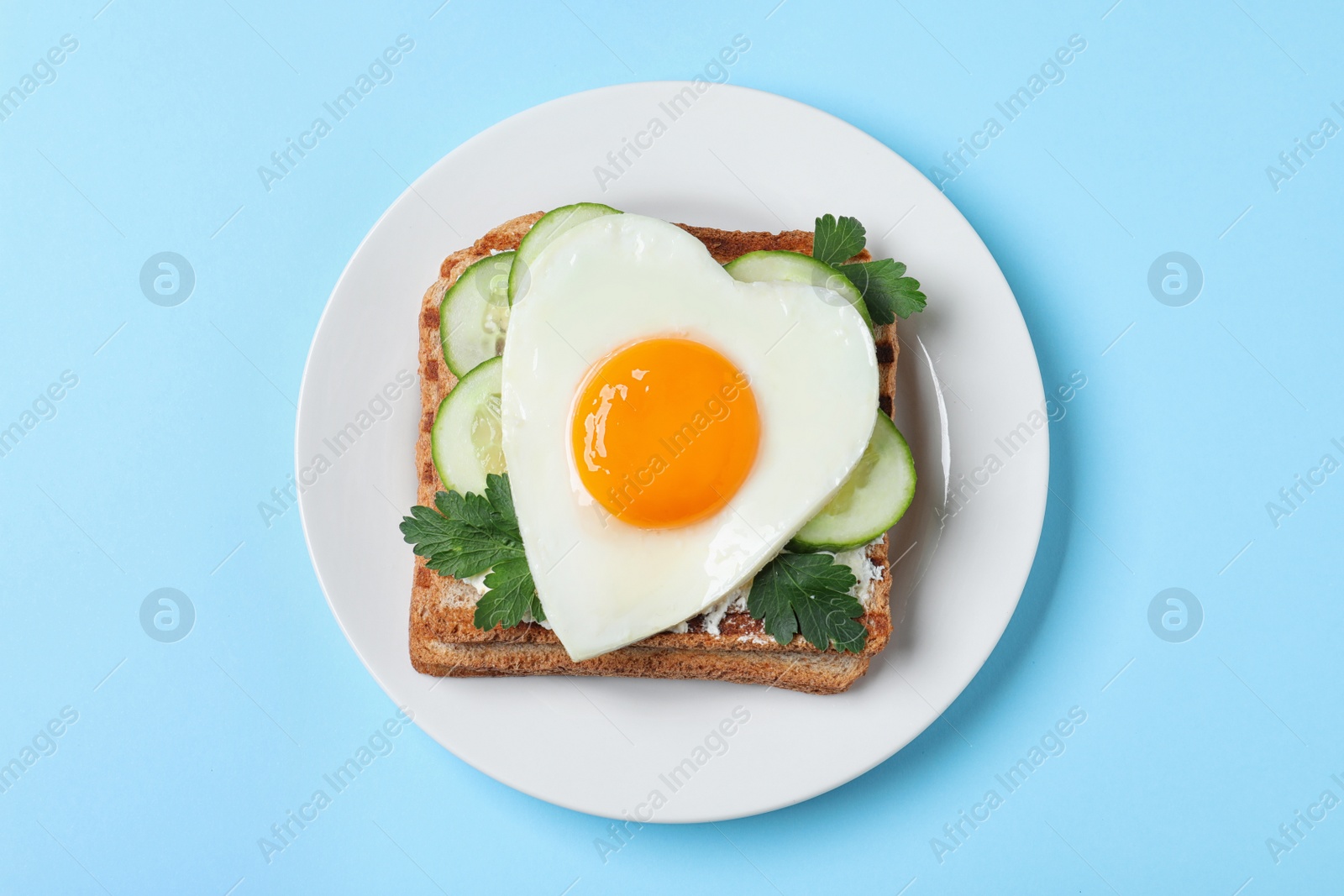 Photo of Plate of tasty sandwich with heart shaped fried egg on light blue background, top view