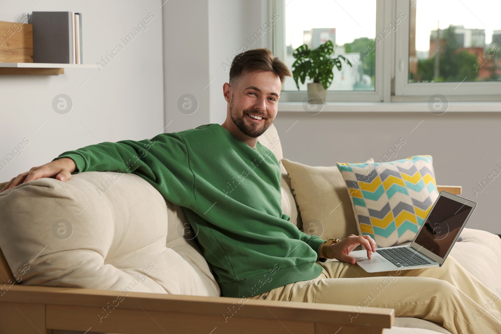 Photo of Handsome man with laptop sitting on sofa at home