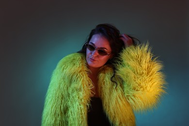 Portrait of beautiful woman in yellow fur coat and sunglasses on dark background with neon lights