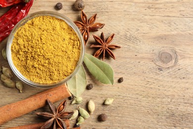 Photo of Curry powder in bowl and other spices on wooden table, flat lay. Space for text