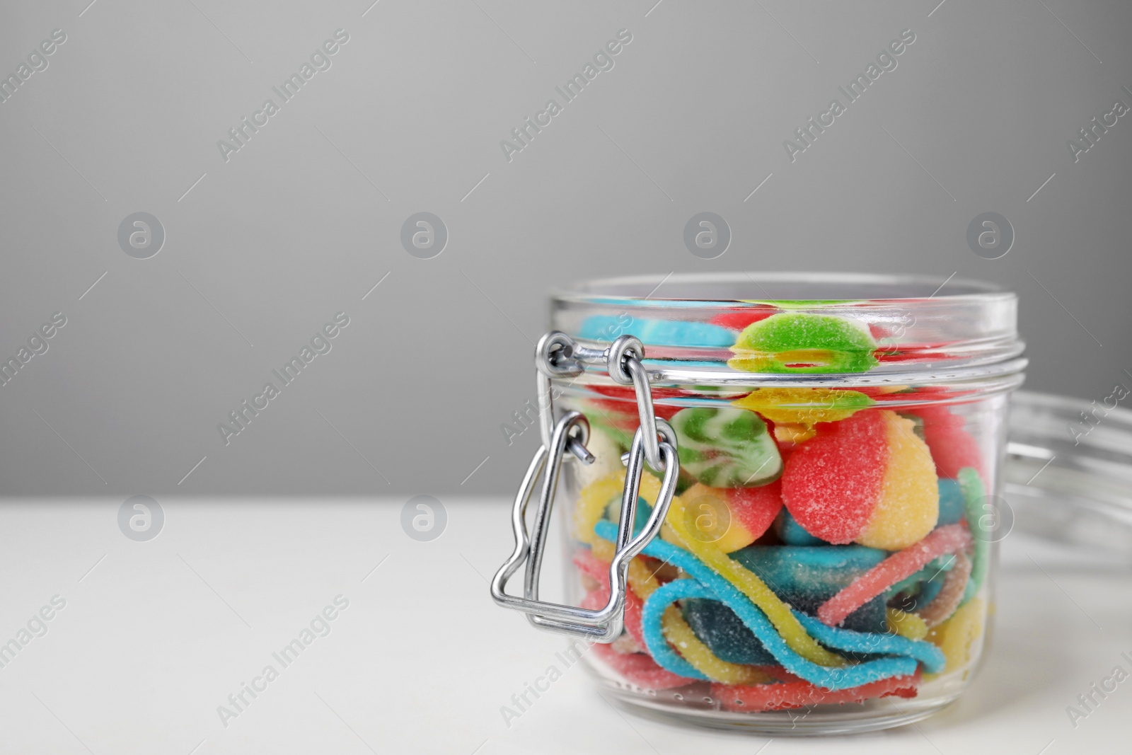 Photo of Tasty jelly candies in open jar on white table, closeup. Space for text