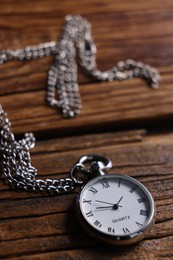 Silver pocket clock with chain on wooden table, closeup