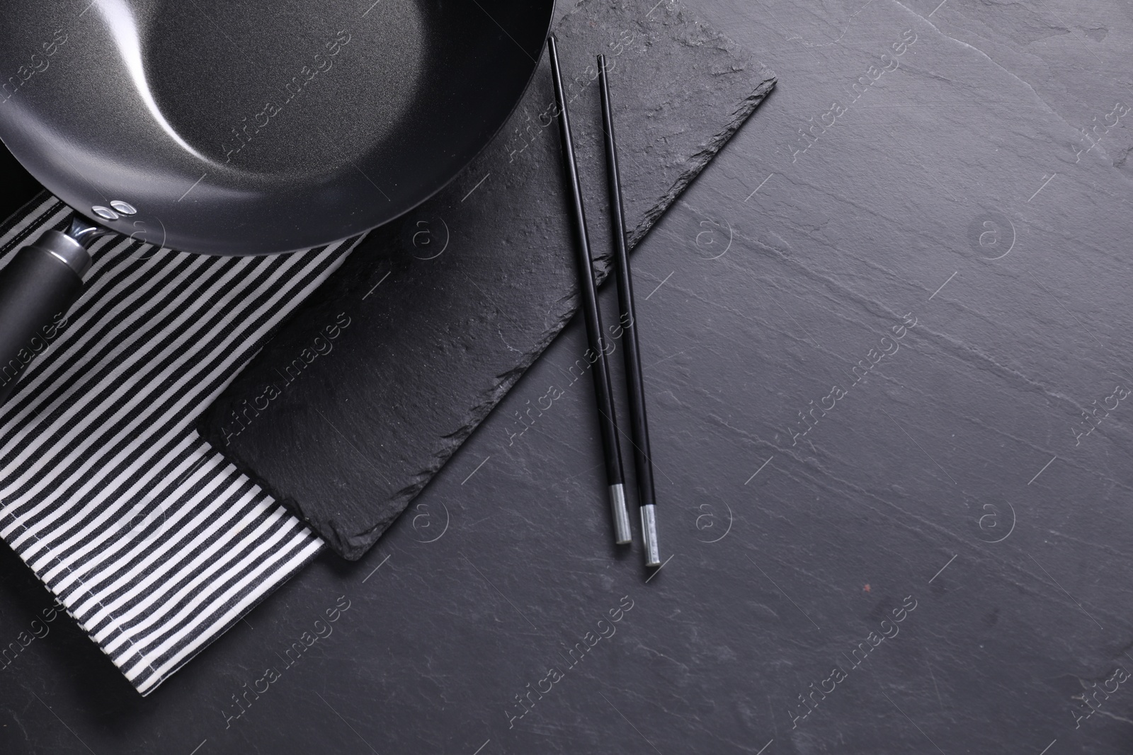 Photo of Empty iron wok and chopsticks on black table, top view. Space for text
