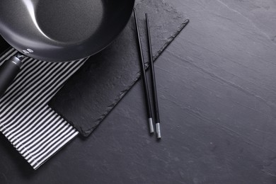 Empty iron wok and chopsticks on black table, top view. Space for text