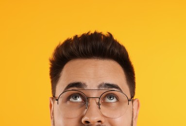 Photo of Man in glasses looking up on orange background, closeup