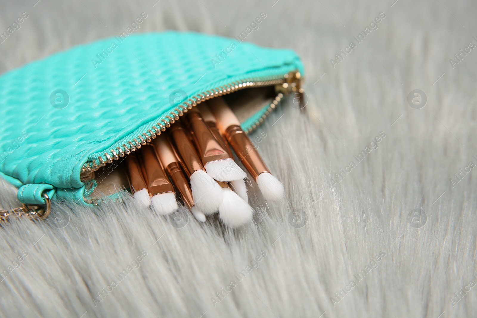 Photo of Bag with set of professional makeup brushes on furry fabric. Space for text