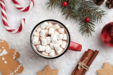 Photo of Hot drink with marshmallows, sweets and festive decor on snow, flat lay