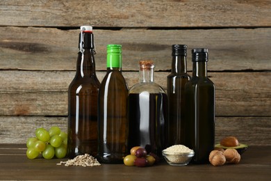 Photo of Vegetable fats. Different cooking oils in glass bottles and ingredients on wooden table