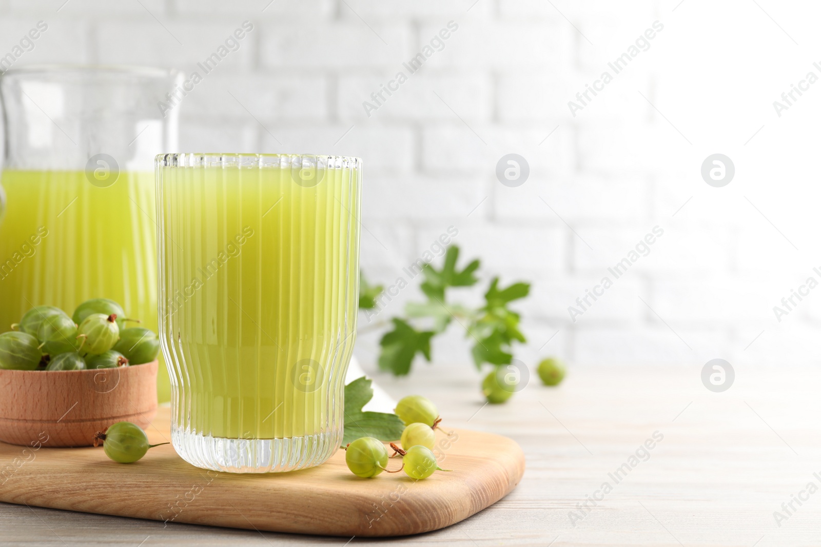 Photo of Tasty gooseberry juice and fresh berries on light wooden table. Space for text