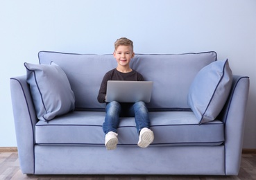 Cute little boy with laptop sitting on sofa, indoors