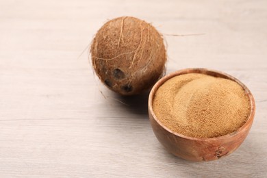 Photo of Coconut sugar in bowl and fruit on light wooden table, closeup. Space for text