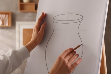 Photo of Woman drawing vase with graphite pencil on canvas indoors, closeup