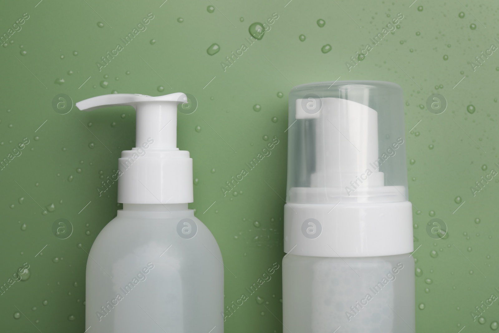 Photo of Wet bottles of face cleansing product on green background, flat lay