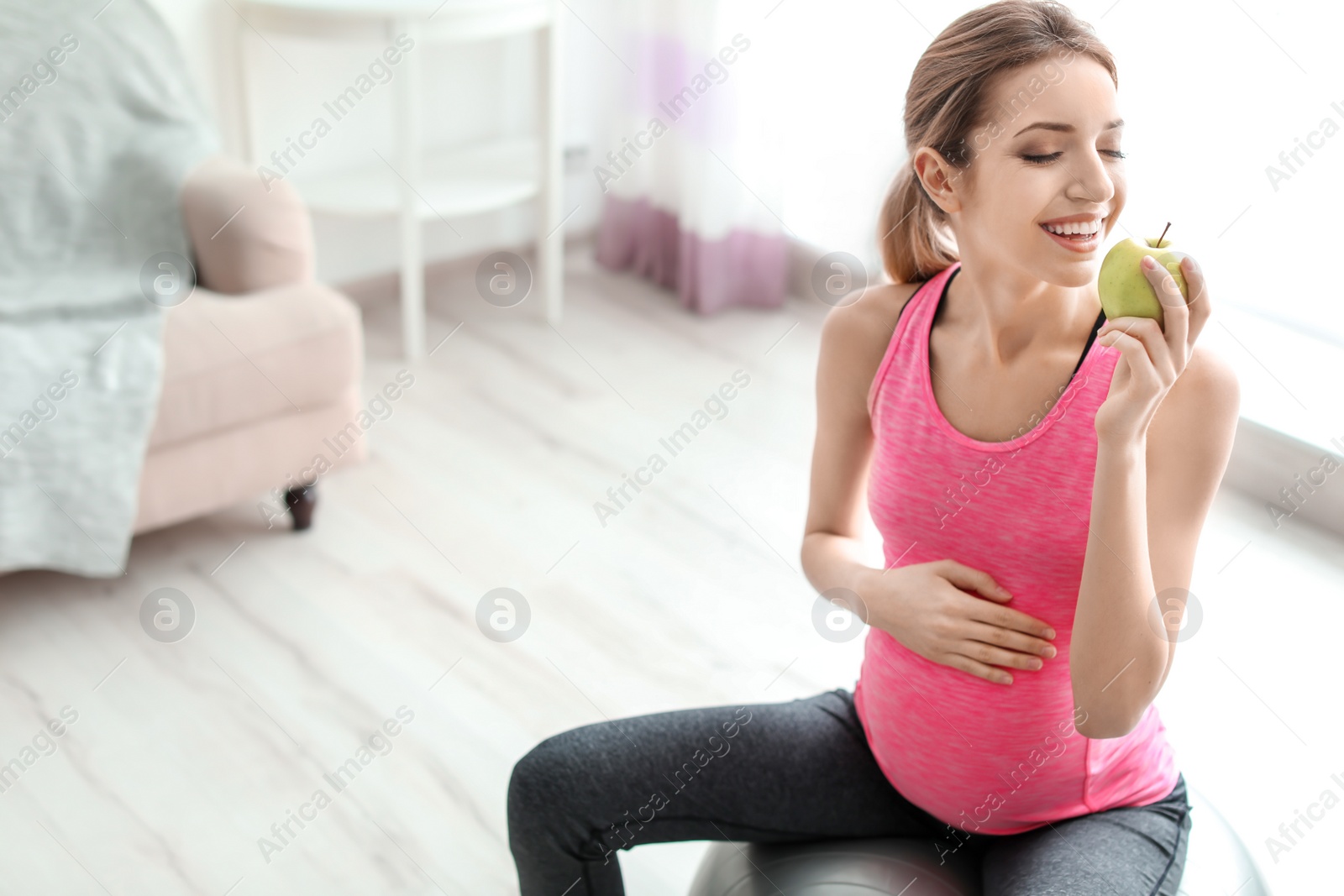 Photo of Young pregnant woman eating apple at home