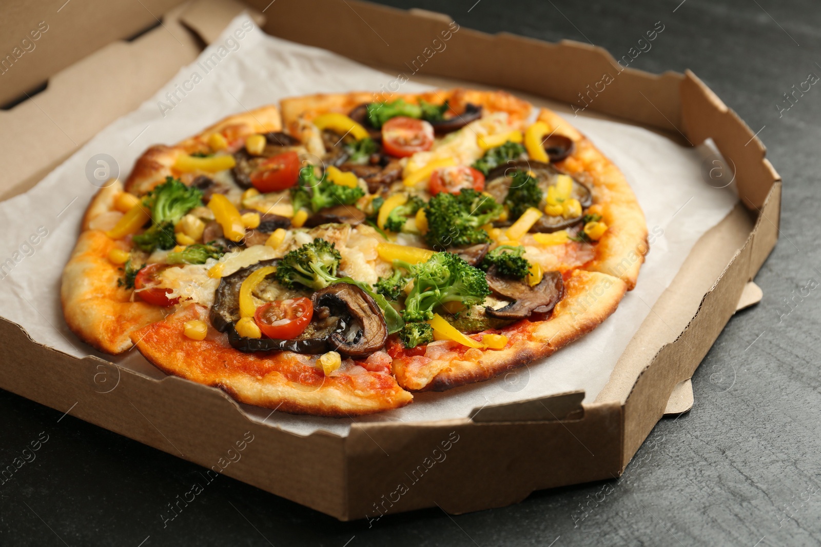 Photo of Delicious vegetarian pizza with mushrooms, cheese and vegetables in box on black table