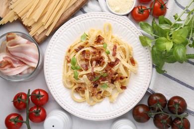 Photo of Tasty pasta with bacon and basil on white marble table, flat lay