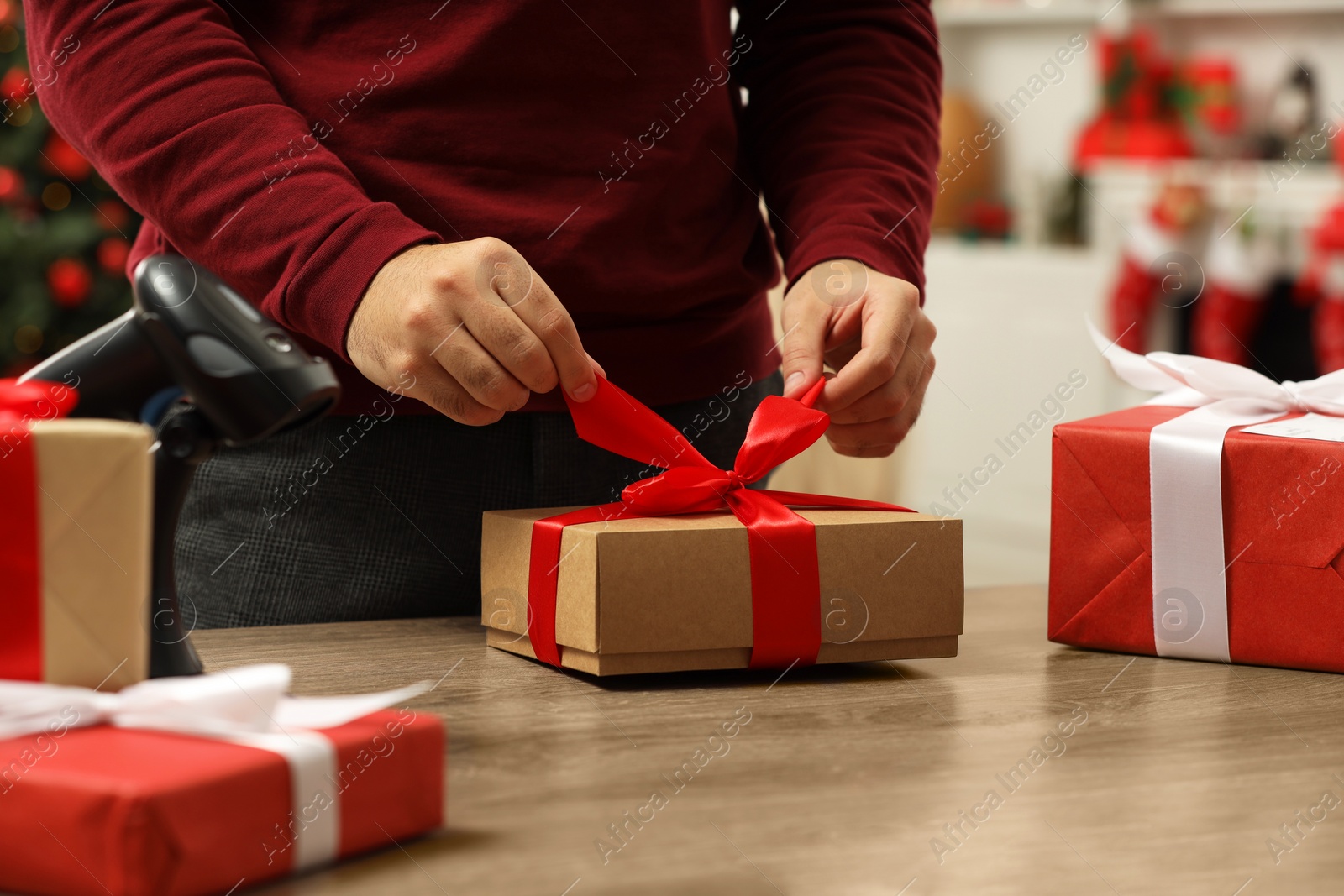 Photo of Man preparing Christmas gift box at wooden table in post office, closeup